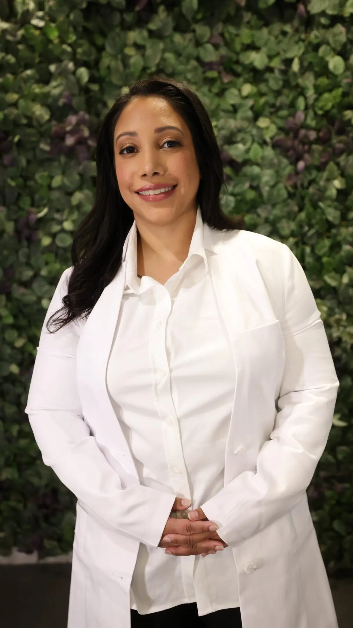 Woman in white coat, green leafy background.