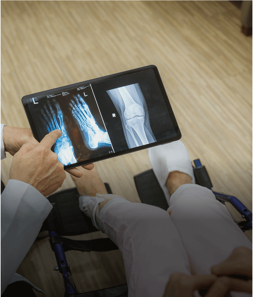 Doctor showing foot and knee X-rays on tablet.